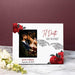 A personalized white photo frame with red roses, skeleton hands, and the phrase “Til Death Do Us Part,” displayed on a marble surface against a dark burgundy background.