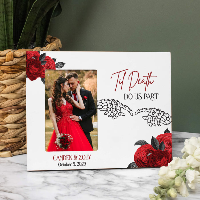 A personalized white wedding photo frame with red roses, skeleton hands, and the text 'Til Death Do Us Part' and 'Canden & Zoey October 5, 2025', displayed on a marble surface next to a woven basket and flowers.