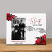A rectangular white photo frame displayed on a wooden surface against a neutral gray background. The picture frame features red roses, skeleton hands, and the text 'Til Death Do Us Part' along with placeholder names and a date.