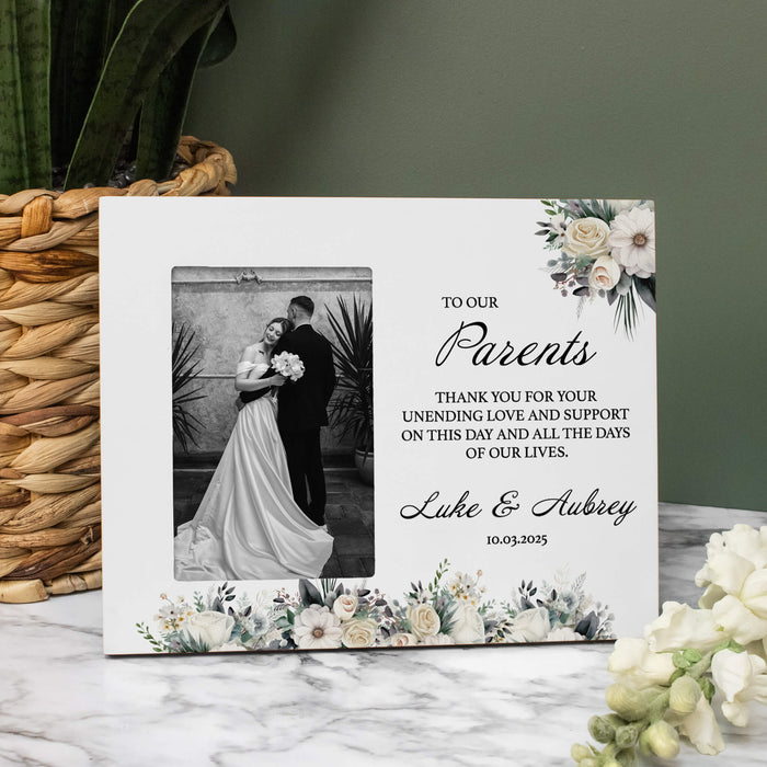 Personalized photo frame with floral design and text for parents on a marble surface.