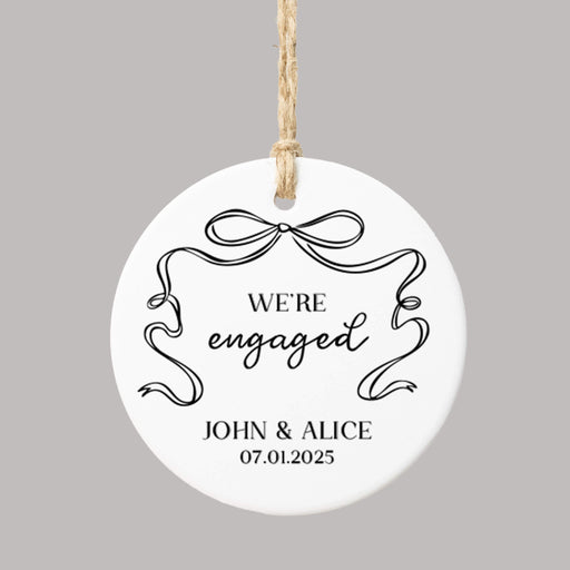 'We're engaged' Christmas ornament personalized with names and a date and decorated with a black coquette bow