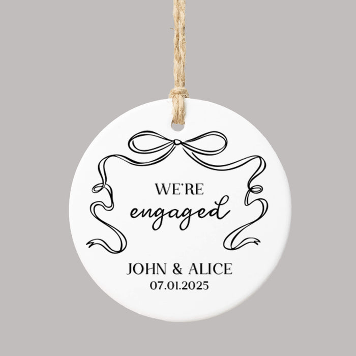 'We're engaged' Christmas ornament personalized with names and a date and decorated with a black coquette bow