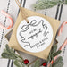 Round white ornament with 'We're Engaged' text on a square brown gift box, surrounded by Christmas decorations.