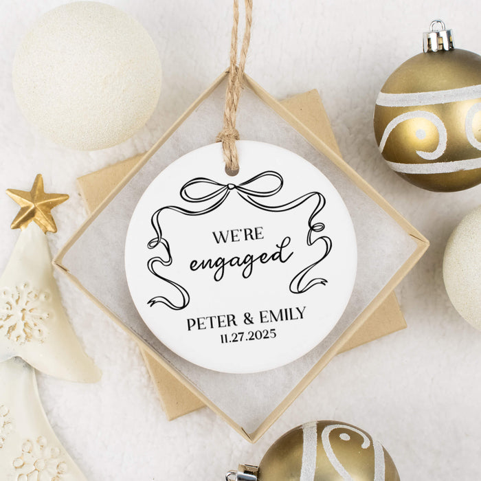 Engagement ornament with 'We're engaged' text and personalized details, surrounded by gold Christmas ornaments.