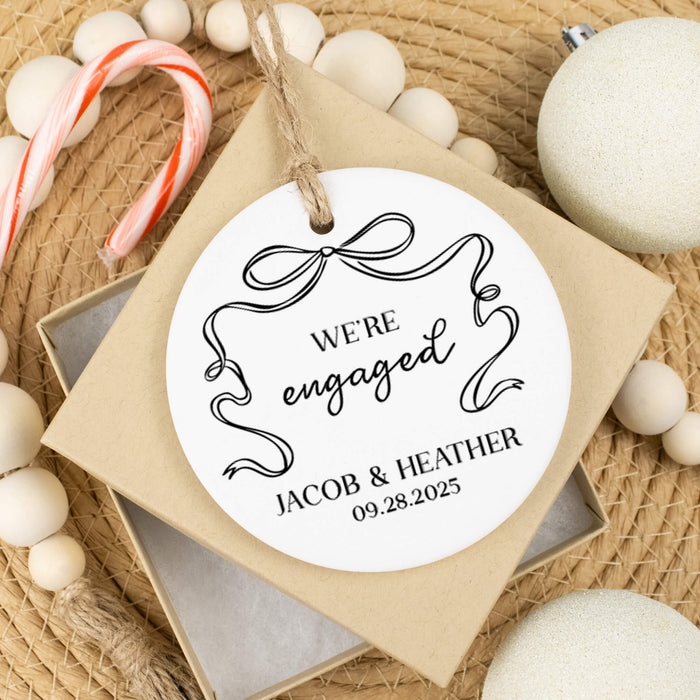 Personalized 'We're Engaged' ornament with decorative elements on a textured surface.