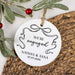 Round white ornament with 'We're engaged' text and personalization on a woven surface with greenery.