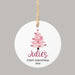 A round white ceramic Christmas ornament with a hanging twine loop, featuring a pink Christmas tree, the personalized name 'Julie's' in dark pink script, and the text 'FIRST CHRISTMAS 2026' below, shown on a solid gray background.