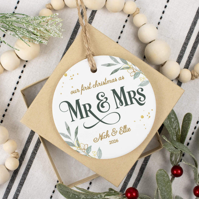 personalized Christmas ornament placed on top of its gift box next to white beads and holly branches on a black and white striped background