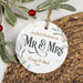 'Our first Christmas as Mr & Mrs' ornament laid on a wicker placemat next to a holly branch