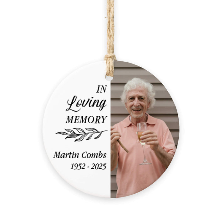 Round hanging memorial ornament with a printed photo of an older man holding a drink on the right side and black memorial text on the left side, suspended by a twine string against a white background.