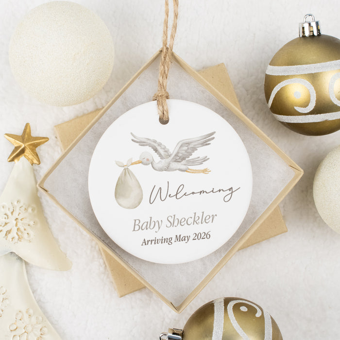 Decorative ornament with baby announcement text, surrounded by Christmas ornaments on a light background