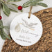 Round ceramic ornament with stork and baby design, text 'Welcoming Baby Uri Arriving March 2026', on a woven surface with mistletoe.