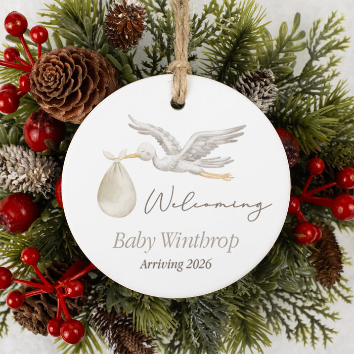 personalized christmas gift ornament with stork and baby announcement text, surrounded by Christmas greenery and berries.