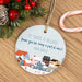 Round Christmas ornament with village scene and personalized text on a wooden surface with festive decorations for a nanny, teacher or babysitter