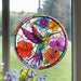Stained glass acrylic suncatcher with a colorful hummingbird and flowers hanging on a window.