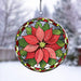 A circular stained-glass style hanging suncatcher featuring a large red poinsettia flower with green leaves and a decorative border, suspended by a chain against a blurred snowy outdoor background.