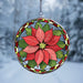 A circular stained-glass suncatcher featuring a red poinsettia flower and green leaves, suspended by a short chain against a blurred snowy outdoor background.