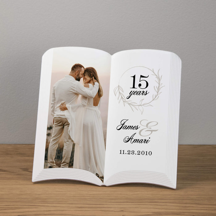 Personalized book-shaped photo plaque with a couple's photo and anniversary details on a wooden surface.