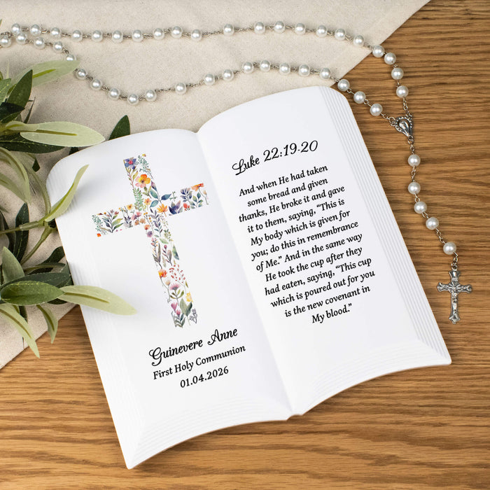Personalized ceramic book with floral cross design and religious text on a wooden surface with a rosary.