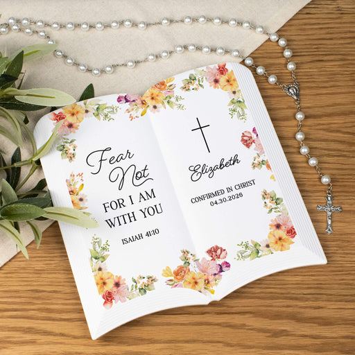 Personalized confirmation book pages with floral design and religious text on a wooden surface.