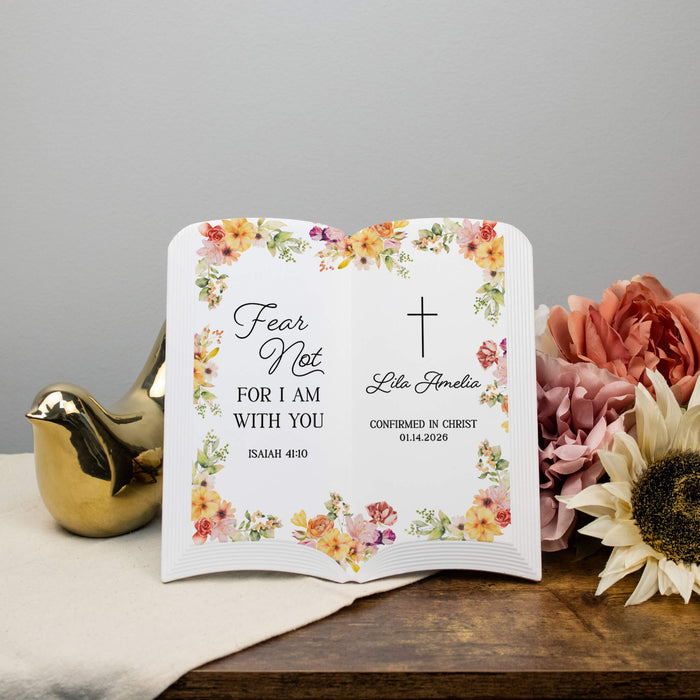Personalized ceramic book pages with floral design and religious text on a wooden surface with flowers and a gold bird ornament.