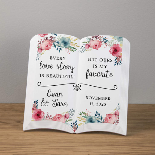 Ceramic open book with floral design and personalized text for a wedding or anniversary on a wooden surface