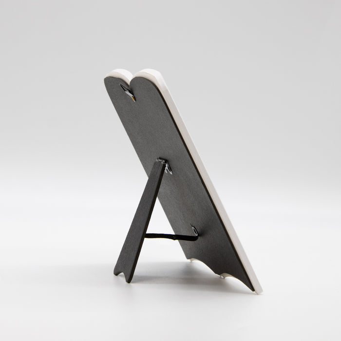 Black stand for a white ceramic book plaque on a light gray background