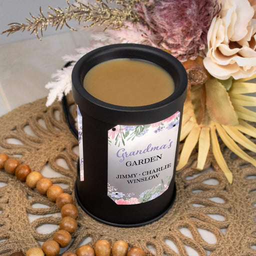 Black metal wax warmer with a decorative label on a textured surface with flowers and beads.