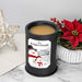 A black cylindrical wax melt lamp with a custom printed label reading 'The Rodgers Family' and a snowman illustration, filled with light tan wax. It sits on a marble surface with holiday decor including a red poinsettia, berries, and a gold star ornament in the background.