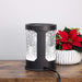 A black cylindrical electric wax warmer with frosted snowflake-patterned panels, shown on a wooden surface next to a potted red poinsettia.