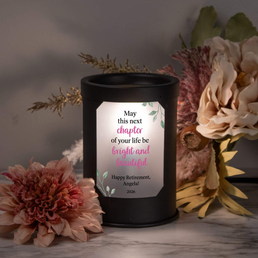 Black wax warmer lamp with a personalized message surrounded by flowers on a marble surface