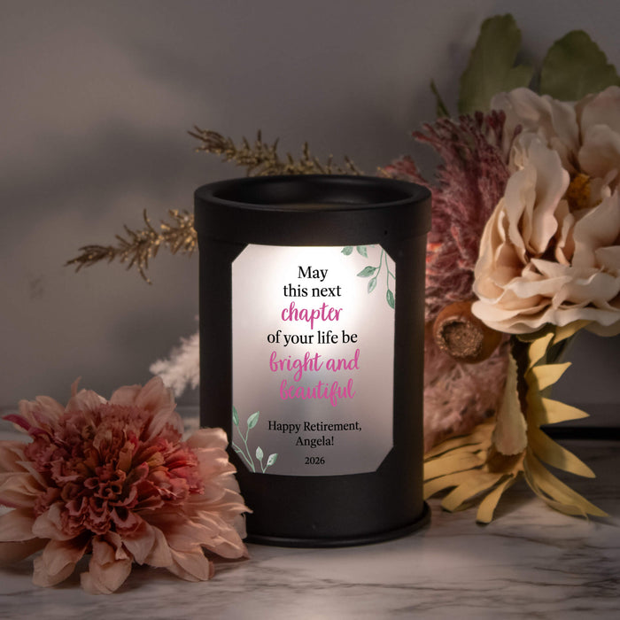 Black wax warmer lamp with a personalized message surrounded by flowers on a marble surface