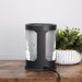 Black cylindrical wax melt lamp with floral design on a wooden surface next to a plant.