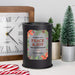 A black cylindrical wax melt lamp with a personalized holiday label reading 'Wishing You PEACE & JOY This Holiday Season The Beckers,' styled on a tabletop with a clock, small potted trees, and candy canes.