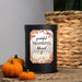 A matte black cylindrical wax warmer with a decorative autumn-themed label reading 'grateful THANKFUL blessed' and a white pumpkin illustration, styled on burlap with small pumpkins and a woven basket in the background