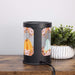 A black cylindrical electric wax warmer with a gray and autumn-themed print featuring pumpkins and fall leaves, shown on a wooden table next to a potted green plant.