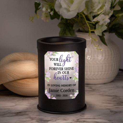 wax warmer turned on to show it lit up with a purple sympathy message and personalized name sitting on a marble table in front of a plant and wooden decor