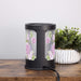 Back of black floral-patterned wax warmer on a wooden surface with a plant in the background