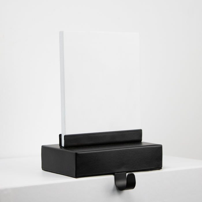 A black stocking hanger hook and white printable plaque, photographed on a clean white surface against a white background.