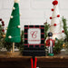 A personalized Christmas stocking hanger stand featuring a black and red plaid pattern with a white center panel and the name 'CAMERON' in red, styled on a wooden shelf with miniature Christmas trees and a nutcracker.