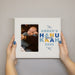 Hands holding a white picture frame featuring a photo of a baby and the name First Hannukah 2025