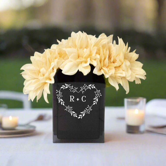 Black Acrylic Vase with a monogrammed heart wreath holding yellow flowers on a table outside