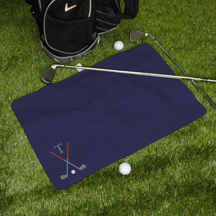 Navy blue monogrammed golf towel with golf club design on grass with golf balls and bag.