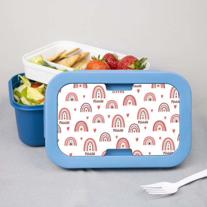 Blue bento box with a personalized rainbow patterned lid containing food on a gray background