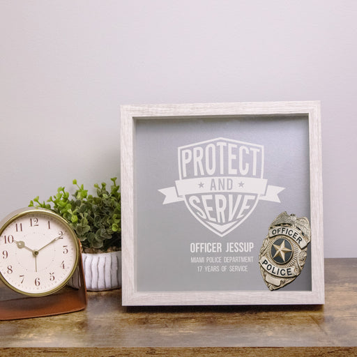 Personalized retirement shadow box with police badge on table next to clock and plant