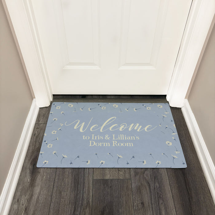 Decorative doormat with 'Welcome to Dorm Room' text on a wooden floor.
