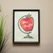 Framed artwork of a red apple with teacher's name on a beige wall.