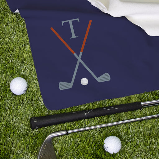 Close up of a navy blue monogrammed golf towel next to golf clubs