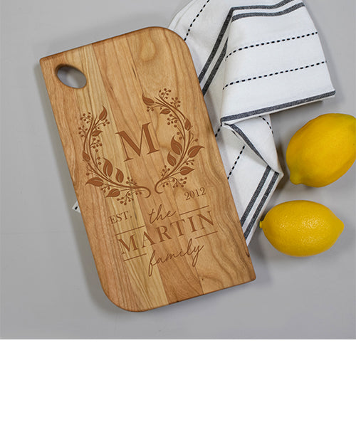 Wooden cutting board with engraved design and text, placed on a gray surface with lemons and a towel.