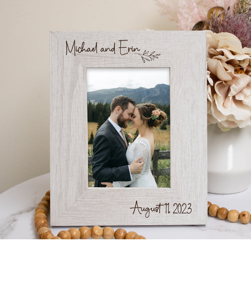 Personalized photo frame with a couple's photo and names, placed on a surface with flowers and beads.